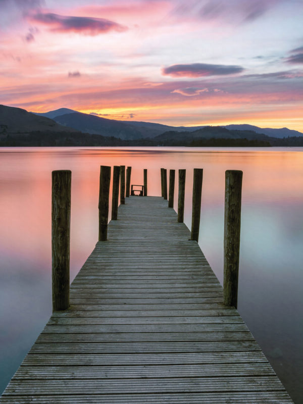 A beautiful vibrant pink and purple sunset with Ashness Jetty in the foreground at Derwentwater in the Lake District, UK.